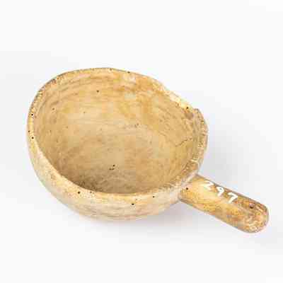 The image shows a worn-looking wooden scoop labelled with the number 297 on its handle. It sits on a white background. / L'image montre une pelle en bois d'aspect usé, dont le manche porte le numéro 297. Elle est posée sur un fond blanc.
