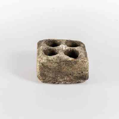 A small, weathered stone block has four circular indentations on its top.  / Un petit bloc de pierre usé par les intempéries présente quatre empreintes circulaires sur sa surface la plus haute.