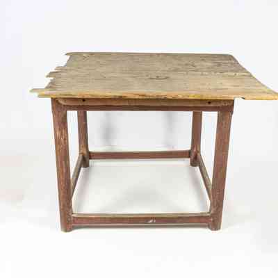The image shows a wooden table with a worn surface and sturdy legs against a plain background. / L'image montre une table en bois à la surface usée et aux pieds solides sur un fond uni.