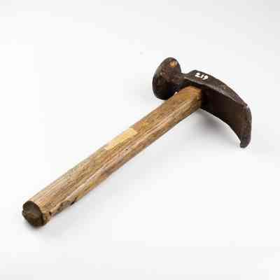 The image displays a weathered hammer with a wooden handle and dark metal head, resting on a plain backdrop. /
L'image montre un marteau usé par le temps, avec un manche en bois et une tête en métal foncé, posé sur un fond uni.