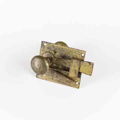 The image depicts a weathered metal door latch featuring a circular knob. / L'image montre un loquet de porte en métal patiné avec un bouton circulaire.