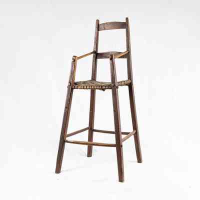 The image shows a wooden high chair with a woven seat, standing alone against a white background. / L'image montre une chaise haute en bois avec un siège tissé, seule sur un fond blanc.