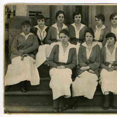 Photograph of 10 nurses sitting on the steps in front of a house