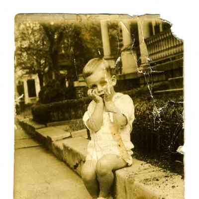 Photograph of a young boy sitting on the side of a sidewalk
