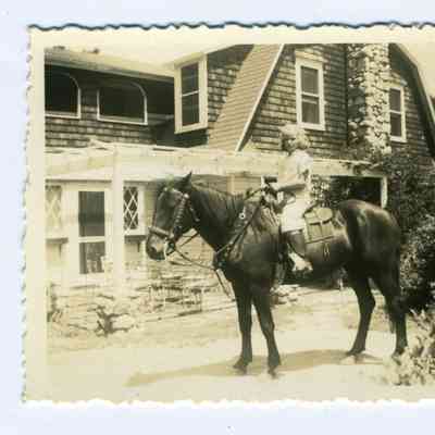 A photograph of a girl on horse in front of a house