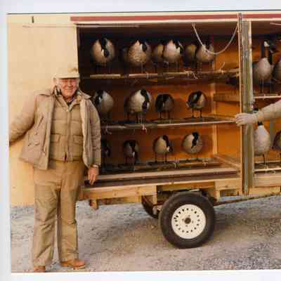 Photograph of two older men in front of a display cart with geese (mounted?)