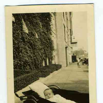 Photograph of a baby in a baby carriage on a city sidewalk