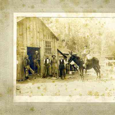 Photograph of 6 men in front of a wooden building