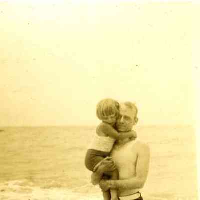 Photograph of a man holding a child in swim ware in the water on a beach