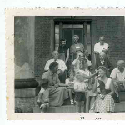 Photograph of 13 people and a dog in front of a brick building, sitting on the steps, September 1955