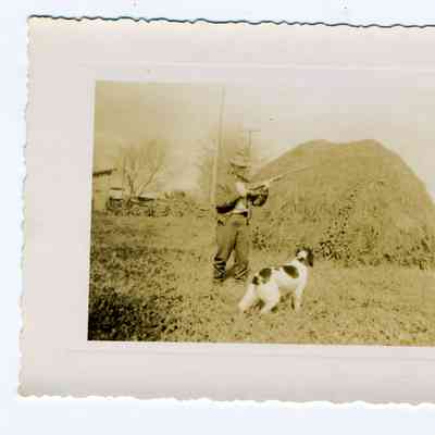 Man with rifle standing in front of a grain mound with a dog