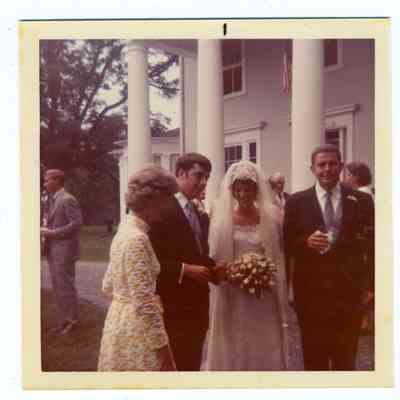 Photograph of a bride and groom among guests in front of t of house