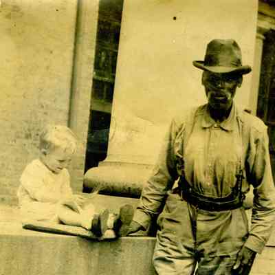 Photograph of a man standing and child sitting on cement platform