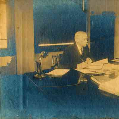 Photograph of a man with mustache in an office working at a desk