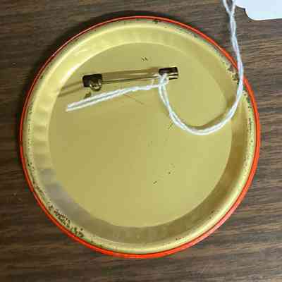 A round pin back displays on the wooden surface, tagged with a string.