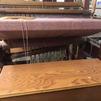The fabric is rolled tightly beneath the main frame of the loom, allowing for a weaver to have easy access to the warp threads through which they may guide the shuttle and the weft thread.
