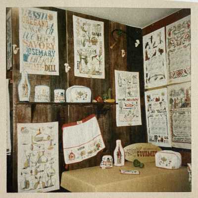 Motif Gourmet line of kitchen soft goods, left wall and table, at a Country Prints trade show booth, 1966 (calendars at right are for 1967).