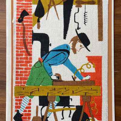 Woodworking: A man planes the face of a large piece of wood in a workshop, with tools of the trade surrounding him, a finished piece of furniture beyond him on the right and a cast iron stove to keep warm in winter behind him. (Six colors)