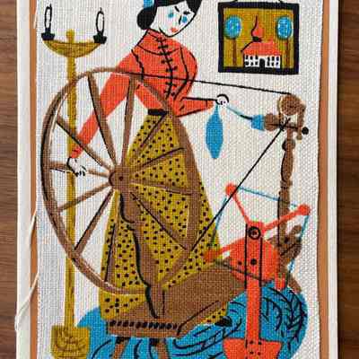 Spinning: A woman spins yarn at a spinning wheel. A tall candle stand is at left. A framed painting of a building with an onion dome hangs on the wall beyond. (Five colors, omits green)