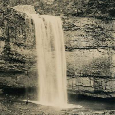 2022.057.007 Recto: Black and white photograph of a man standing at the bottom of Lula Falls