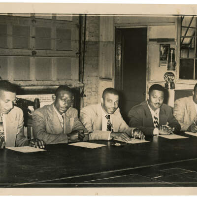 2022.024.004 Recto: Black and white photograph of five men signing papers at Boone Higgins Trade School