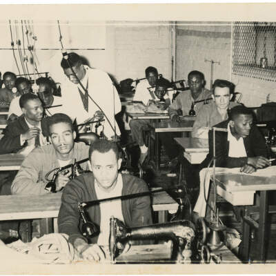 2022.024.012 A Recto: Black and white photograph of men sitting at sewing machines at Boone Higgins Trade School