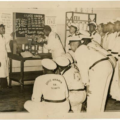 2022.024.007 Recto: Black and white photograph of an instructor at Boone Higgins Trade School discussing paint color with students.