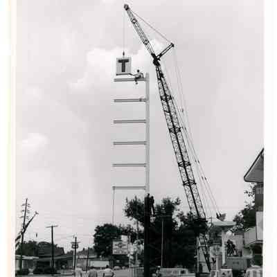 2022.057.012 Recto: Black and white photograph of men installing a sign