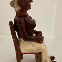 Carving of woman sitting in a chair (2 pieces) at a spinning wheel.