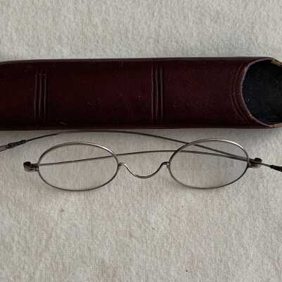 Oval nickel plated eyeglasses in imitation red leather case, late 1890s, early 1900s
