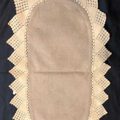 Oval doily of unbleached linen with hand crocheted lace edging, c. 1920s