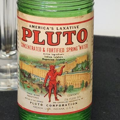 Display case of Averill Family-Owned Items - Close up 1: Pluto Concentrated and Fortified Spring Water bottles label close-up.