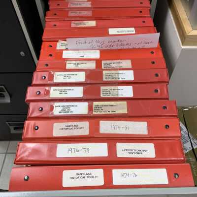 SLHS-FC4 D2: Stores about 14 binders.  The first 8 binders store copies of SLHS newsletters (Historical Highlights and predecessor versions) and clippings and photocopies of SLHS program presentation announcements from 1974 to approximately 2000.  The last 6 binders store various history-related newspaper clippings from publications located throughout the Capital District and are of little interest to SLHS.  All 14 binders were compiled by Sand Lake Town Historians rather than SLHS and donated to SLHS by Town Historian Robert Moore in 2021.