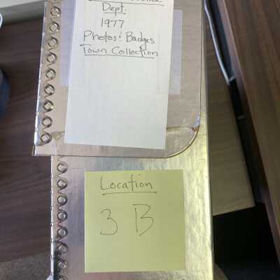 Archive box that contains a binder that stores and preserves the Photos and Badges: The box is located on Shelf 3B in the Town Historian's Storeroom.  Note that the shelf contains two rows of archive boxes and the Photos and Badges box may be stored in the back row and not immediately visible.