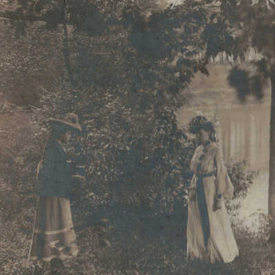 Ladies Alongside the Lake: Ladies alongside the lake postcard.  Features two well and formally dressed ladies in fancy hots.