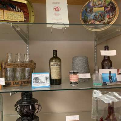Various Artifacts and Photos Display - Right Side Close Up 2nd Shelf: Various Artifacts and Photos Display - Left Side Close Up 2nd Shelf.  Includes a six pack of Sand Lake Springs Bottles, Dr. Wright's Drug Store apothecary bottles, Averill Park souvenir glass,  Faith Mills spool of yarn, and artifacts recovered during the construction of the Rite Aid Drug Store (now Walgreens) in West Sand Lake.