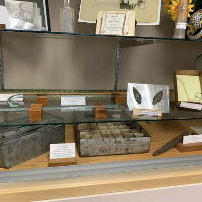 Various Artifacts and Photos Display - Left Side Close Up Bottom Shelves - 1: Various Artifacts and Photos Display - Left Side Close Up Bottom Shelves -1.  Includes glass canes, a glass pipe, Native American Artifacts, egg mailers, and two Troy and New England Railroad Trolley spikes.