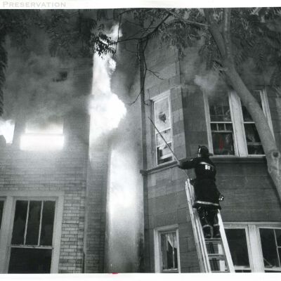 Firefighter on ladder attempting to break out windows