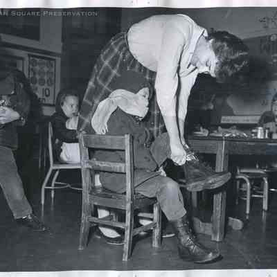Mrs. Sonia Augerin, teacher putting boots on Tommy Paris