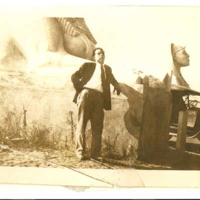 Man poses in front of 2 sphinx taken from the set of The Ten Commandments with old car in the background.