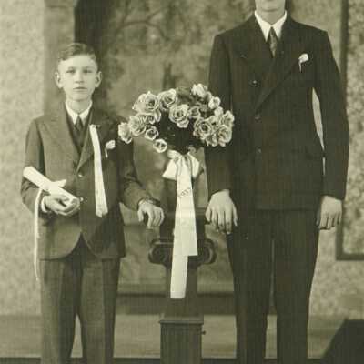 Two Young Men Standing Next to Vase of Flowers "1932" Stitched in Ribbon