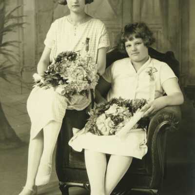 Two Young Ladies Sitting on Chair Holding Bouqets of Flowers and Rolled Papers (Diplomas?)