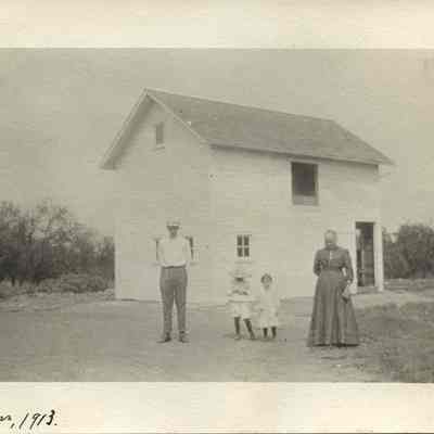 A man, two children, and woman in front of white barn. The photo is captioned "The New Barn, 1913." The woman is most likely Louisa Litzel, and the children are likely Agnes and Wallace Litzel.