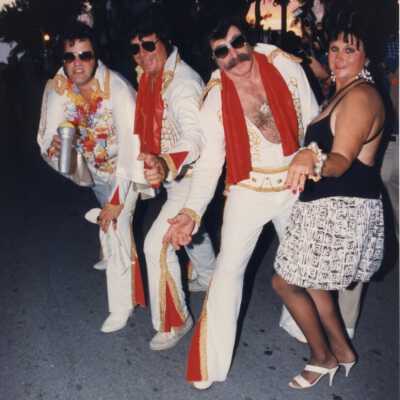 Three unknown men dressed as Elvis with an unknown woman.