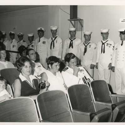 Unknown people sitting and standing in a room, some in uniform