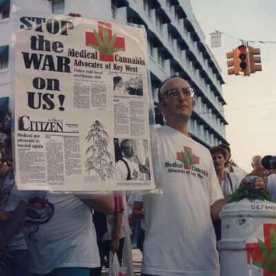 Unknown man standing in front of La Concha holding a sign that reads Stop the war on us.