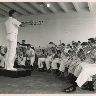 Men in uniform playing instruments in a band while one is directing