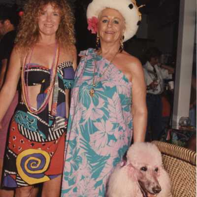 Unknown woman dressed up standing with a pink poodle.