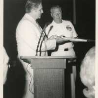 2 Unknown men at a podium, one is receiving an item