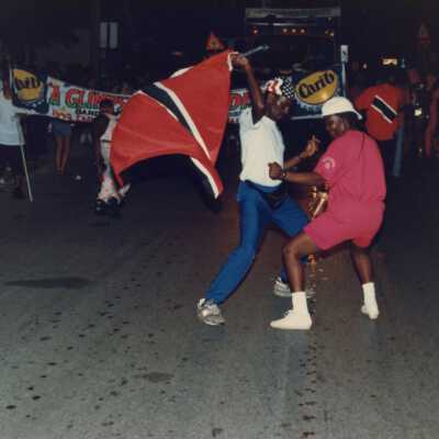 Two unknown people dancing on the parade, one is holding a flag.